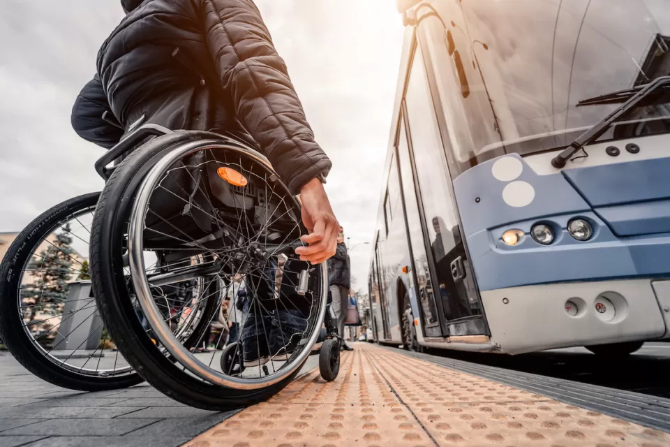 Ground-up view of man using wheelchair waiting to board a light blue bus.